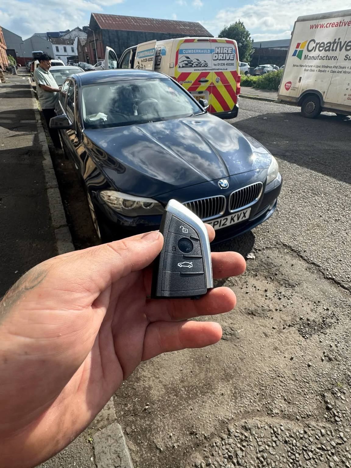 BMW key held in front of a dark blue BMW 5 Series